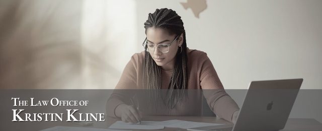 Woman with glasses reviewing documents at desk with laptop, representing the Law Office of Kristin Kline, specializing in family law services in Houston.